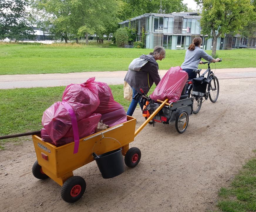 Fahrrad mit Fahrradanhaenger wird geschoben, der Waste-Buster ist eingehaengt und wird mitgezogen.