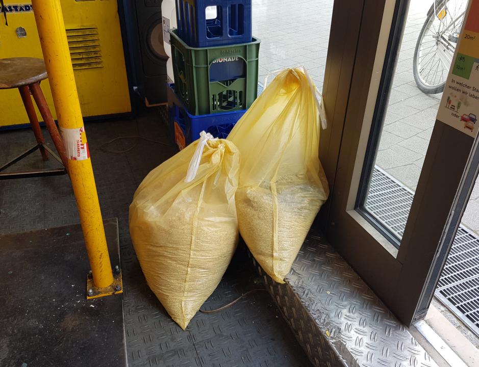 Zwei Saecke mit Hobelspaenen neben der Eingangstuer des zwanzig°.